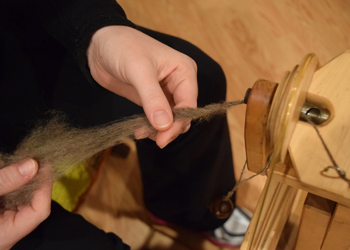 closeup of hand spinning thread on spinning wheel